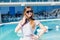 Young pretty girl with long hair and in black sunglasses is standing near pool. She wears gray T-shirt and skirt. She