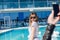 Young pretty girl with long hair and in black sunglasses is standing near pool. She wears gray T-shirt. Somebody hand