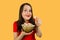 Young pretty girl with opened mouth and wide eyes holds glass bowl with popcorn isolated on orange background