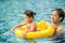 Young pretty girl playing in yellow swimming ring with her mother in pool with clear water.