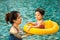Young pretty girl playing in yellow swimming ring with her mother in pool with clear water.