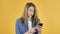 Young Pretty Girl in Shock while Using Smartphone on Yellow Background