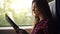 Young, pretty girl travelling by modern train. Sitting next to the window and reading in plaid shirt. Side view. Blurred