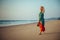 Young pretty girl walking along the seashore and admires the sunset. Blonde in bright clothes on sandy beach in the light of