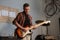 A young pretty guitarist plays guitar in a garage at a band rehearsal.