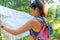 Young pretty hiker woman with backpack holding map in summer forest. Active lifestyle concept