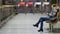 Young pretty lady sits on wooden bench in spacious lit lobby with smartphone