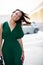 Young pretty likable cheerful woman posing summer city outdoor. Beautiful self-confident girl dressed in emerald-colored jumpsuit