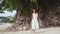 Young pretty smiles woman with long hair in white drees walks on a tropical beach