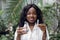 Young pretty smiling African American woman scientist agronomist wearing white lab coat, posing to camera in greenhouse