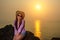 Young pretty smiling woman in straw hat, sunglasses and pink shirt sits on a rock against the sea and sky. Solar path on the water