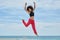 Young pretty sportswoman jumping on beach raising hands