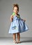 Young pretty toddler girl kid with big sweet lollypop candy in blue dress on grey