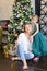 Young pretty woman with bengal light wearing jeans and sitting with daughter near Christmas tree.