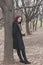 Young pretty woman in black coat outdoor lean on tree in park full body shot winter autumn