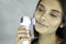 Young pretty woman doing skin care procedure. Cleaning face on grey background. copy space