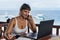 Young pretty woman freelancer writer working with laptop notepad and phone in front of blue tropical sea