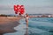 Young pretty woman holding red and white balloons and walking at the sand beach. Copy space