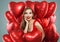 Young pretty woman holds red balloons. Surprised model girl with red lips makeup, perfect curly hairstyle and cute smile. Gifts,