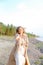 Young pretty woman with outstretched hand on shingle beach wearing summer coat.