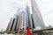 Young pretty woman in red dress and straw hat pointed with hands on downtown skycrapers in modern city. Low angle view