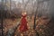 Young pretty woman in the red dress is walking in the foggy mystical forest