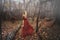 Young pretty woman in the red dress is walking in the foggy mystical forest