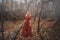 Young pretty woman in the red dress is walking in the foggy mystical forest