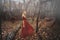 Young pretty woman in the red dress is walking in the foggy mystical forest