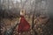 Young pretty woman in the red dress is walking in the foggy mystical forest
