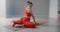 Young pretty woman in red sports tracksuit sits on the twine and demonstrates stretching and yoga exercises in slow