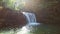 young pretty woman sitting and looking at waterfall at autumn sunny day