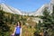 A young pretty woman smiling along a hiking trail with a huge mountain in the background during a sunny day in autumn