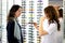 Young pretty woman is trying sun glasses on at an eyewear shop with help of a shop assistant