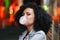 Young pretty woman with very curly afro hair inflates a bubble ball of white chewing gum at night. Trendy girl having