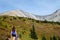 A young pretty woman walking along a hiking trail towards a huge mountain in the background during a sunny day in autumn