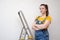 Young Professional repairwoman with a brush for painting on background ladder and gray cement wall. Independent single