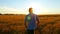 A young promising farmer walks across a field of wheat toward the sunset. Harvest concept.