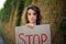 Young protesting woman in white shirt and jeans holds protest sign broadsheet placard with slogan `Stop` for public