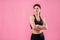 Young pumped up girl coach posing in the studio on a pink background. Dressed in a black top and black pants. Feeling very relaxed