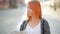 The young red-haired female tourist attentively considers the map. The girl walks streets of the old European city.