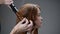 A young red-haired girl curls her hair with a curling iron.