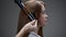 A young red-haired girl curls her hair with a curling iron.