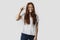 Young red-haired girl isolated on gray background in white t-shirt. Shows a gesture with his hands small price. The concept of a