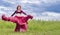 Young red-haired girl in red dance dress dances on green meadow against blue summer sky.