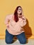 Young red haired overweight woman in stylish hoodie and jeans is posing on floor sending us a kiss