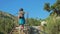 Young red-haired traveler girl with a cowboy hat and a backpack climbs stairs in a mountainous area.