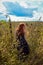 Young red-haired woman from behind is standing in a field with tall grass