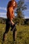 Young red-haired woman in casual wear with thermos in hands in the field, walking