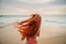 Young red-haired woman with flying hair on the ocean, rear view